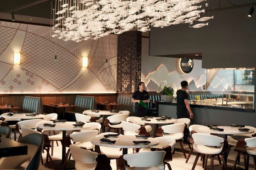Main dining hall lined with marble like top round base dining table, FH222835DCWH PU leather upholstered crescent chair and fish pendant chandelier overhead
